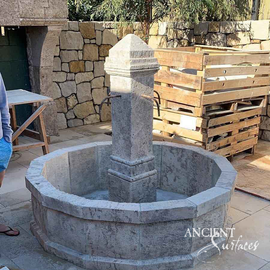 Twelve-sided grey limestone pool fountain with a square center pillar and forged spouts