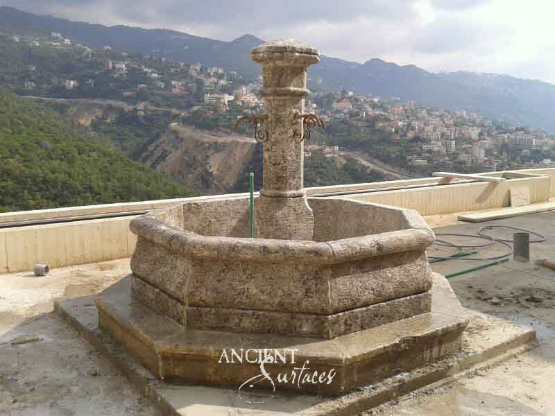 Hexagonal golden limestone pool fountain with a columned center and bronze spouts on a raised plinth