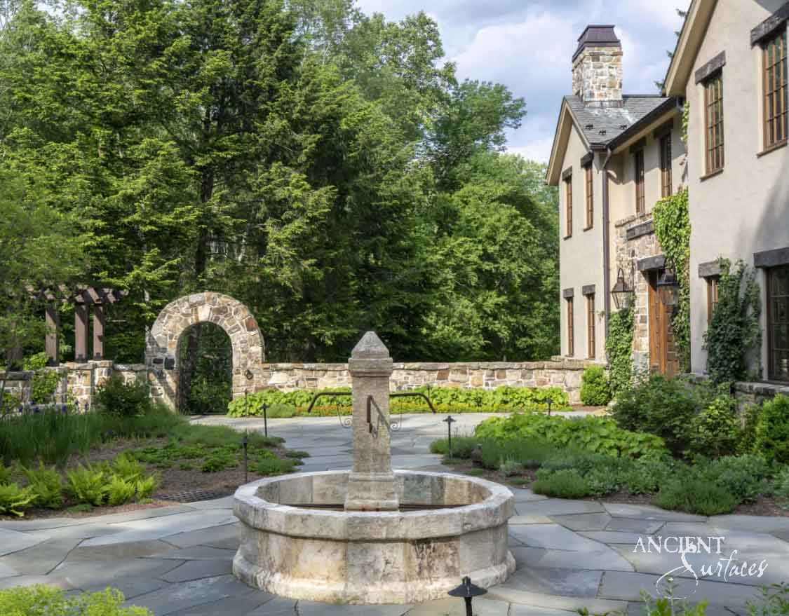 Reclaimed limestone garden fountain on a bluestone terrace beside a stone estate home
